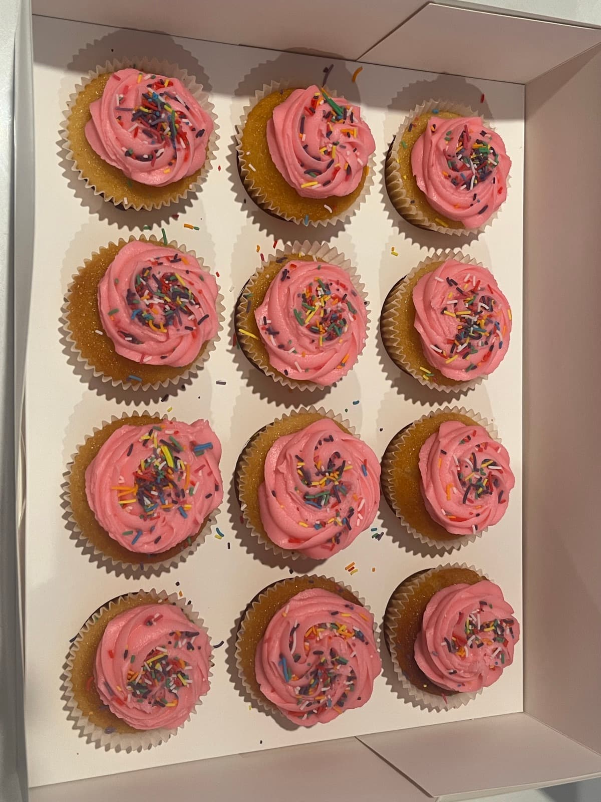 Pink buttercream cupcakes covered in rainbow sprinkles